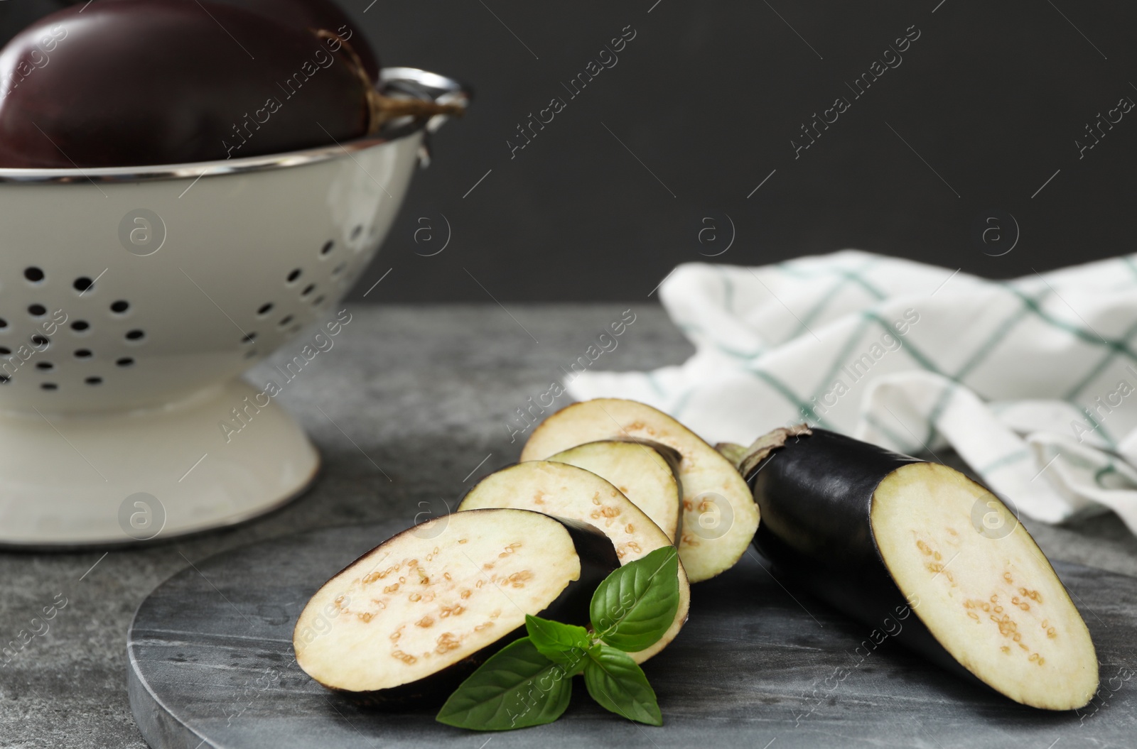 Photo of Cut purple eggplant and basil on grey table, closeup