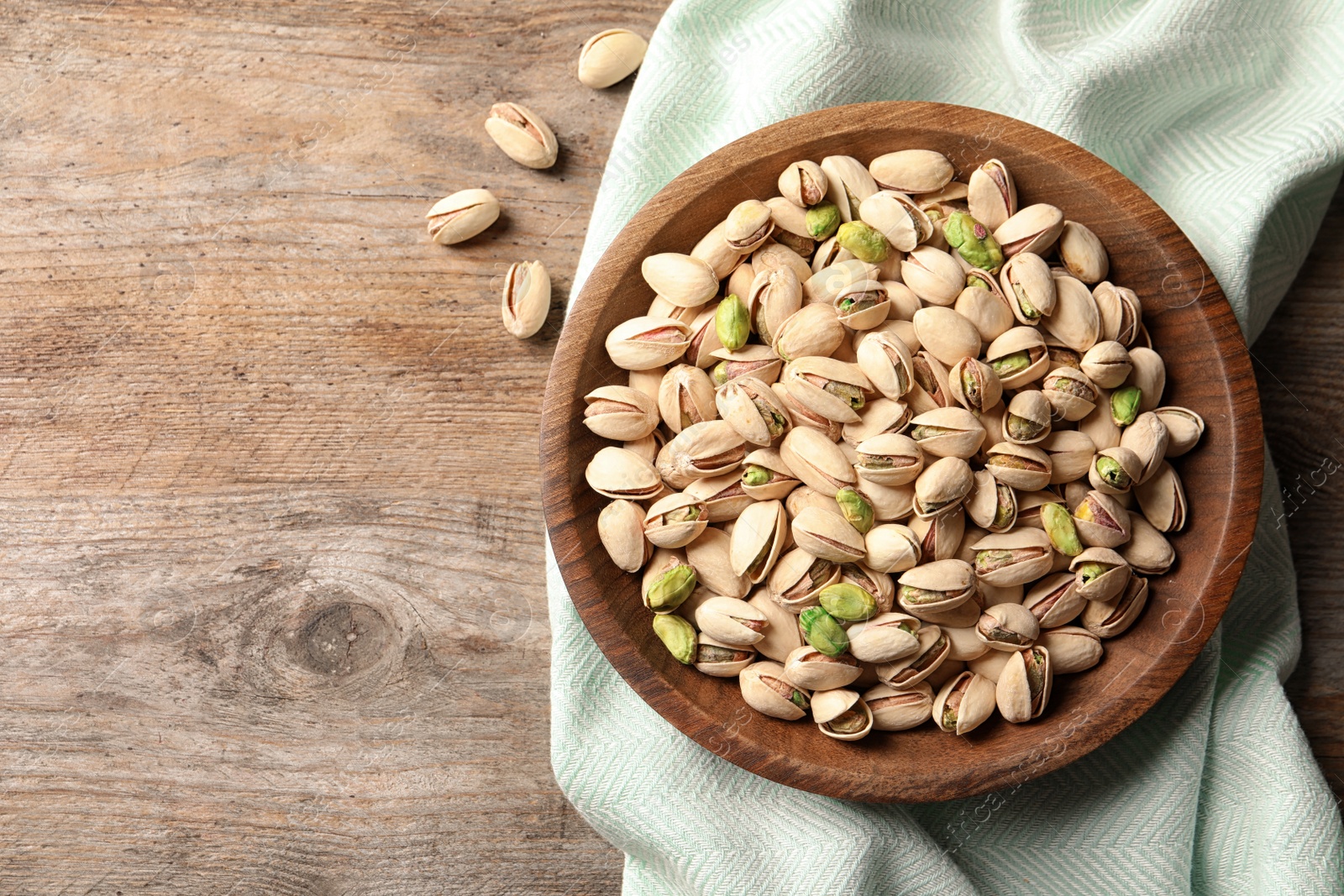 Photo of Organic pistachio nuts in bowl on wooden table, top view. Space for text