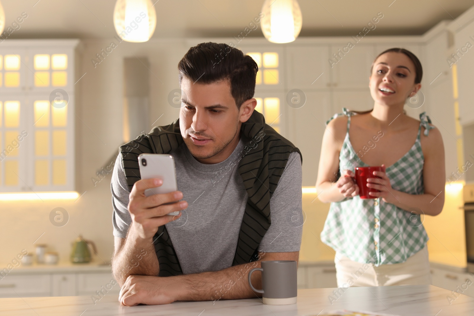 Photo of Distrustful woman peering into boyfriend's smartphone at home. Jealousy in relationship