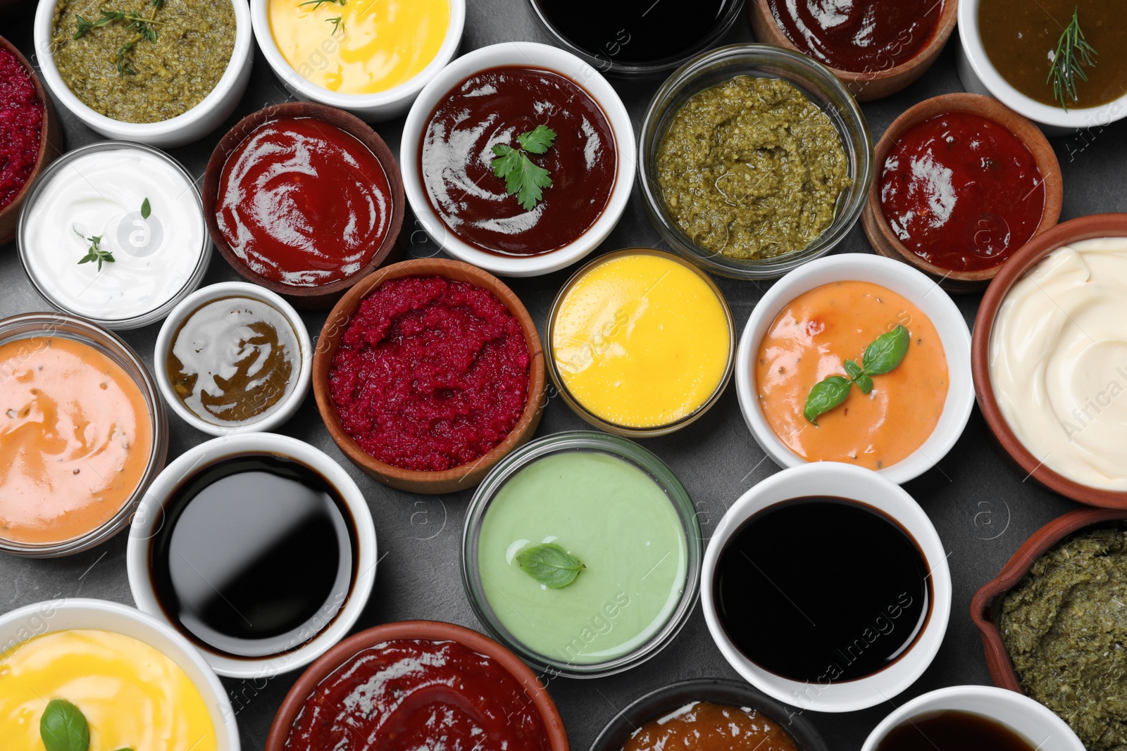 Photo of Many different sauces and herbs on black table, flat lay