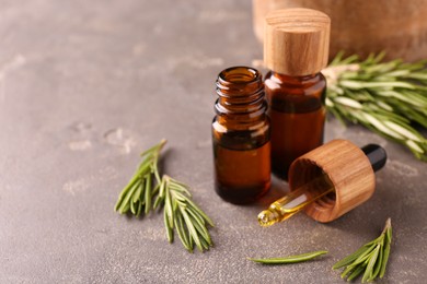 Essential oil in bottles, dropper and rosemary on grey table, space for text