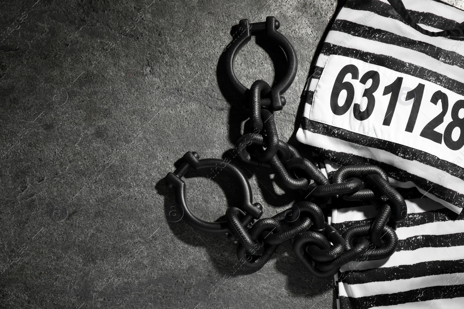 Photo of Steel shackles and jail clothes on grey table, flat lay. Space for text