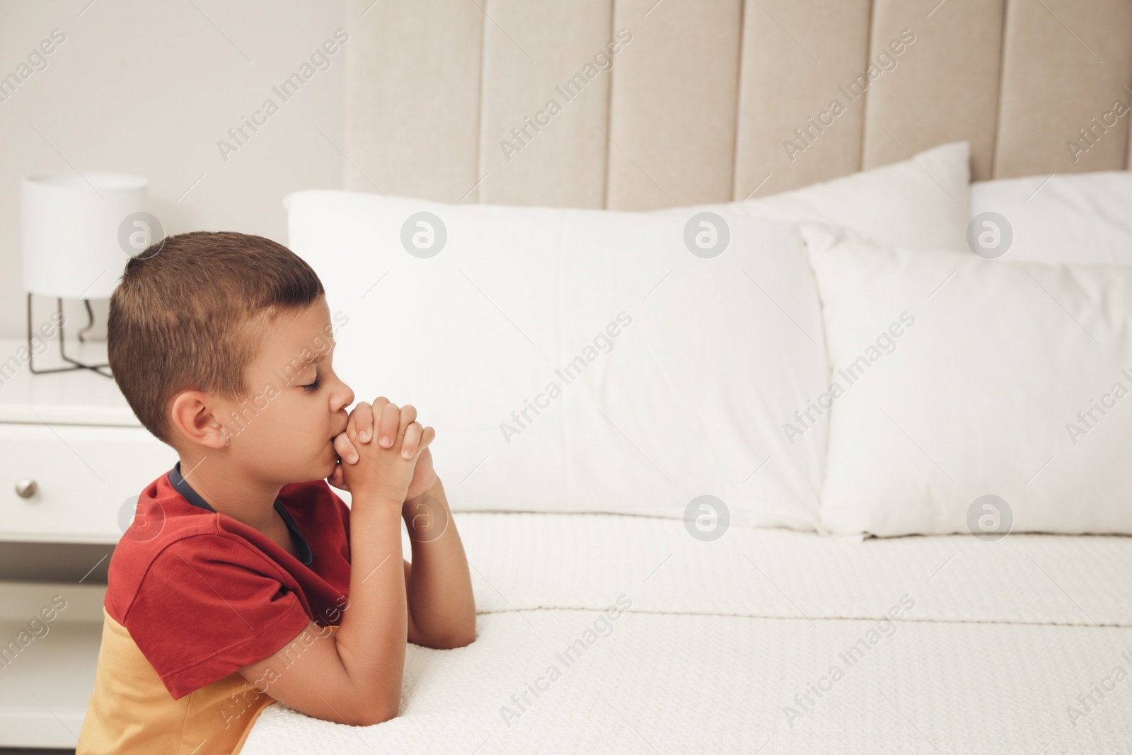 Photo of Cute little boy with hands clasped together saying bedtime prayer at home. Space for text