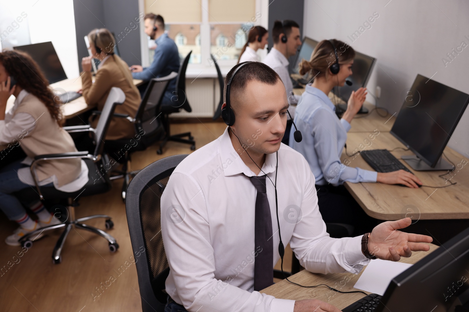 Photo of Call center operators working in modern office, focus on young man with headset