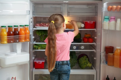 Photo of Cute little girl choosing food in refrigerator at home