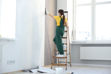 Woman smoothing stylish gray wallpaper in room