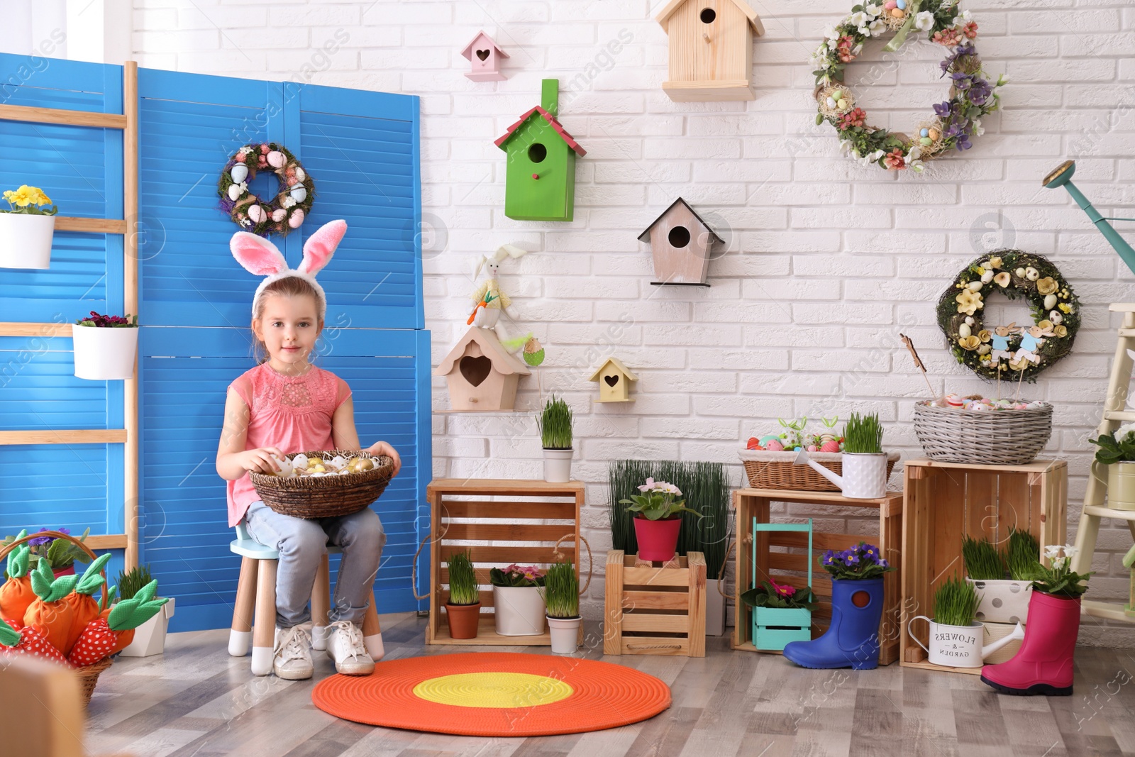 Photo of Adorable little girl with bunny ears and basket full of dyed eggs in Easter photo zone