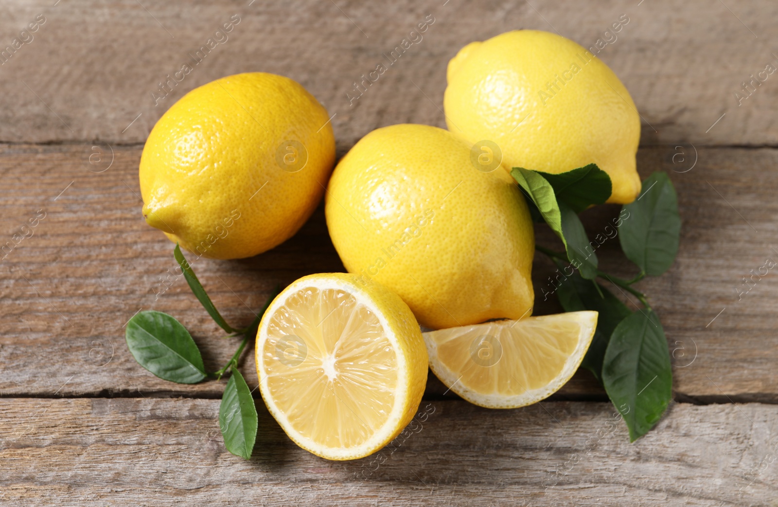 Photo of Fresh lemons and green leaves on wooden table, closeup