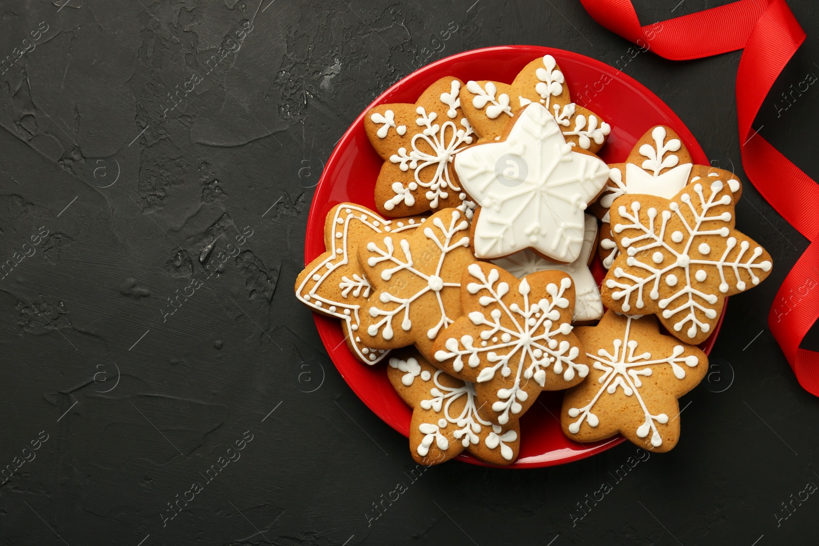 Photo of Tasty Christmas cookies with icing and red ribbon on black table, top view. Space for text