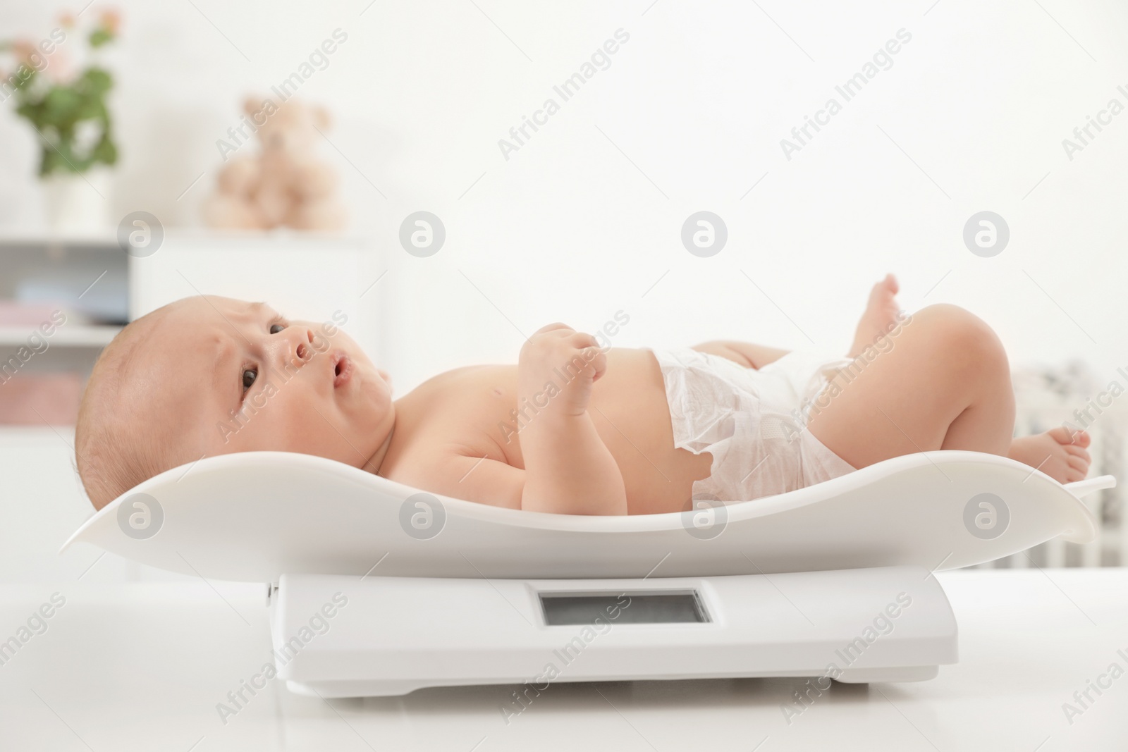 Photo of Cute little baby lying on scales in light room