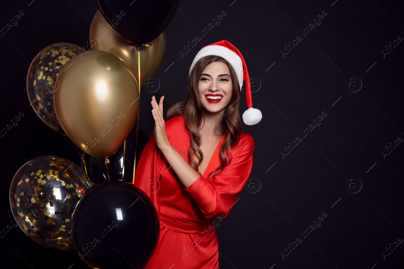 Photo of Happy woman in Santa hat with air balloons on black background, space for text. Christmas party
