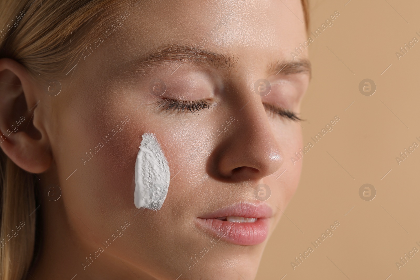 Photo of Beautiful young woman with sun protection cream on her face against beige background, closeup