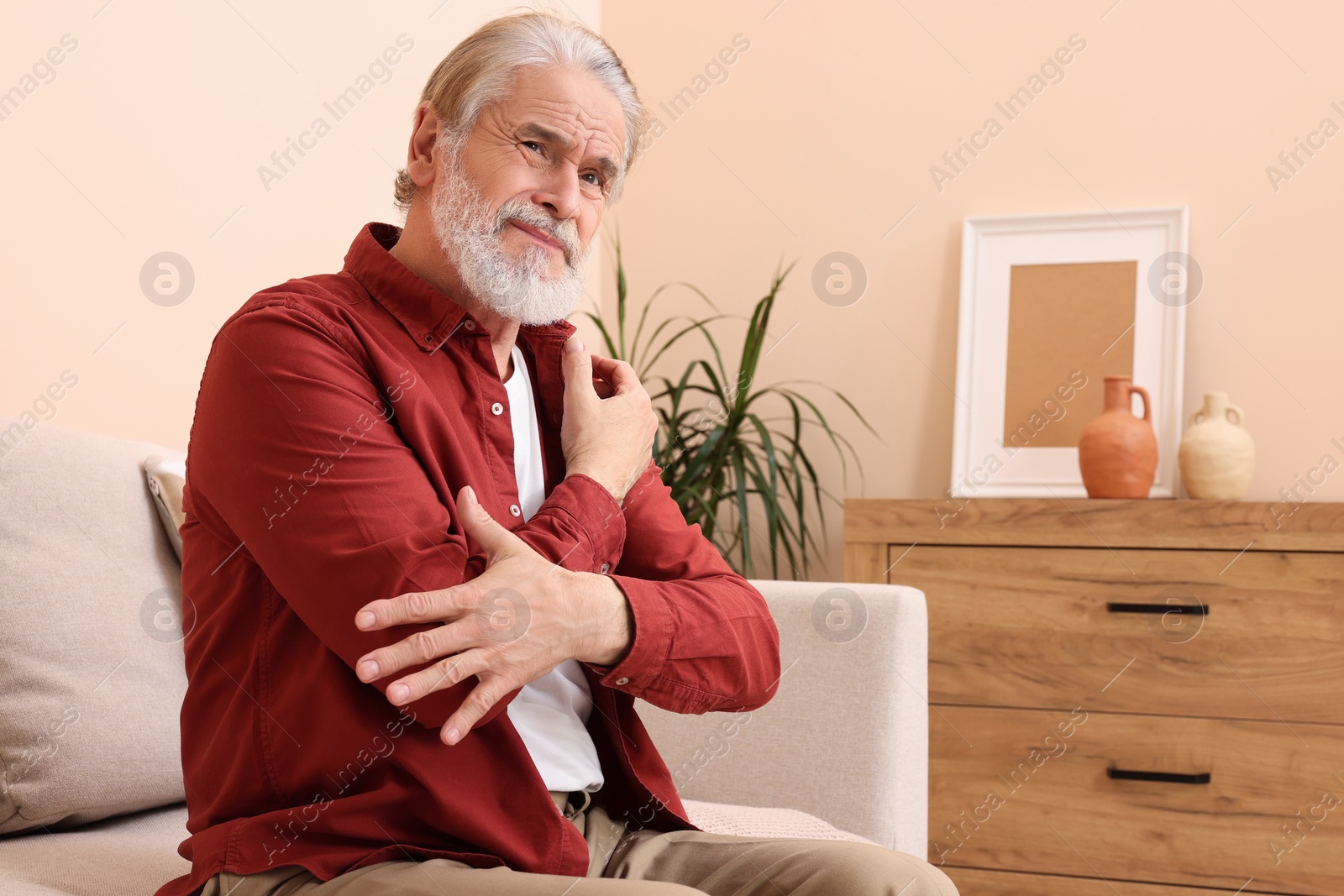 Photo of Senior man suffering from pain in his hand at home. Arthritis symptoms