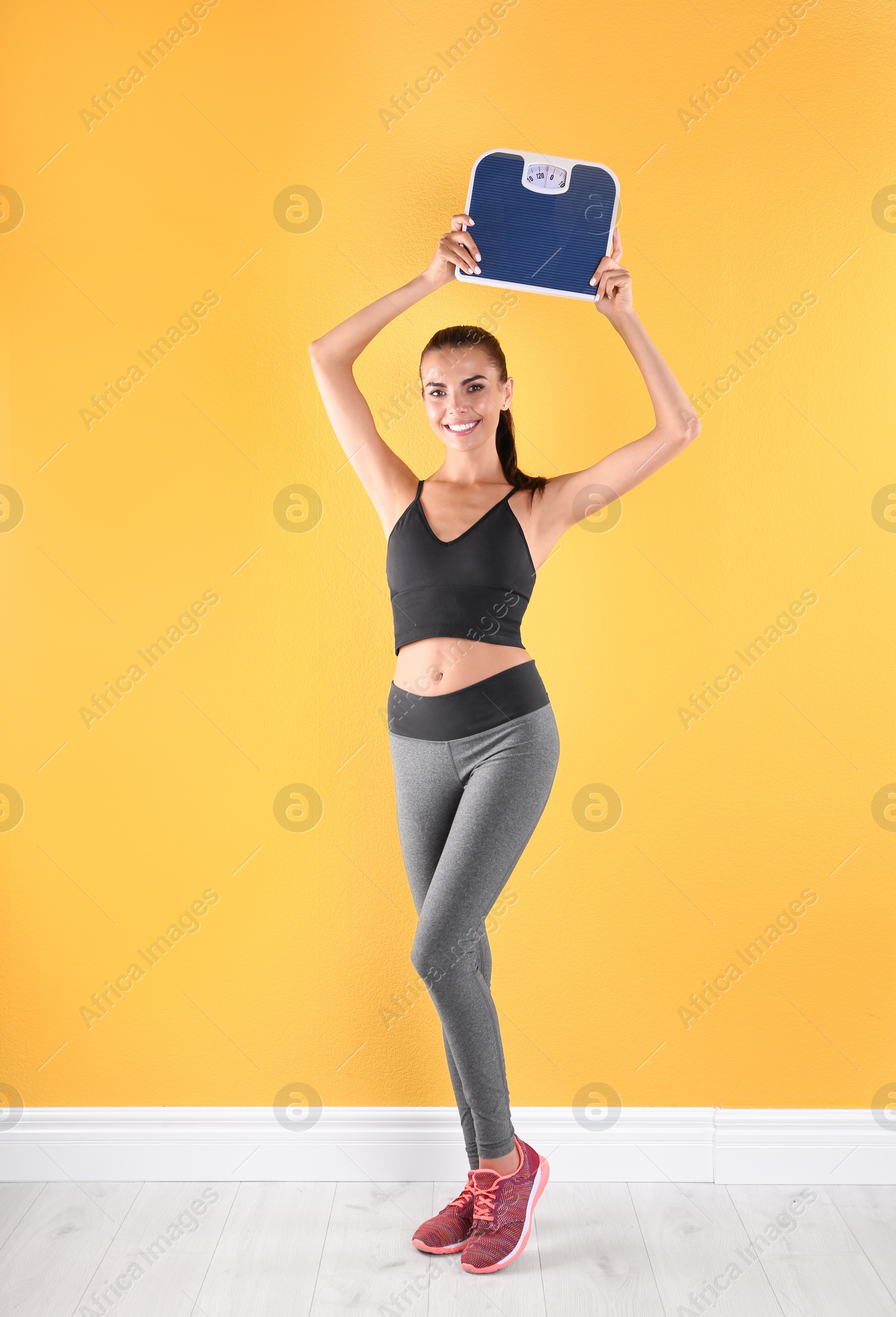 Photo of Happy young woman with scales near color wall. Weight loss motivation