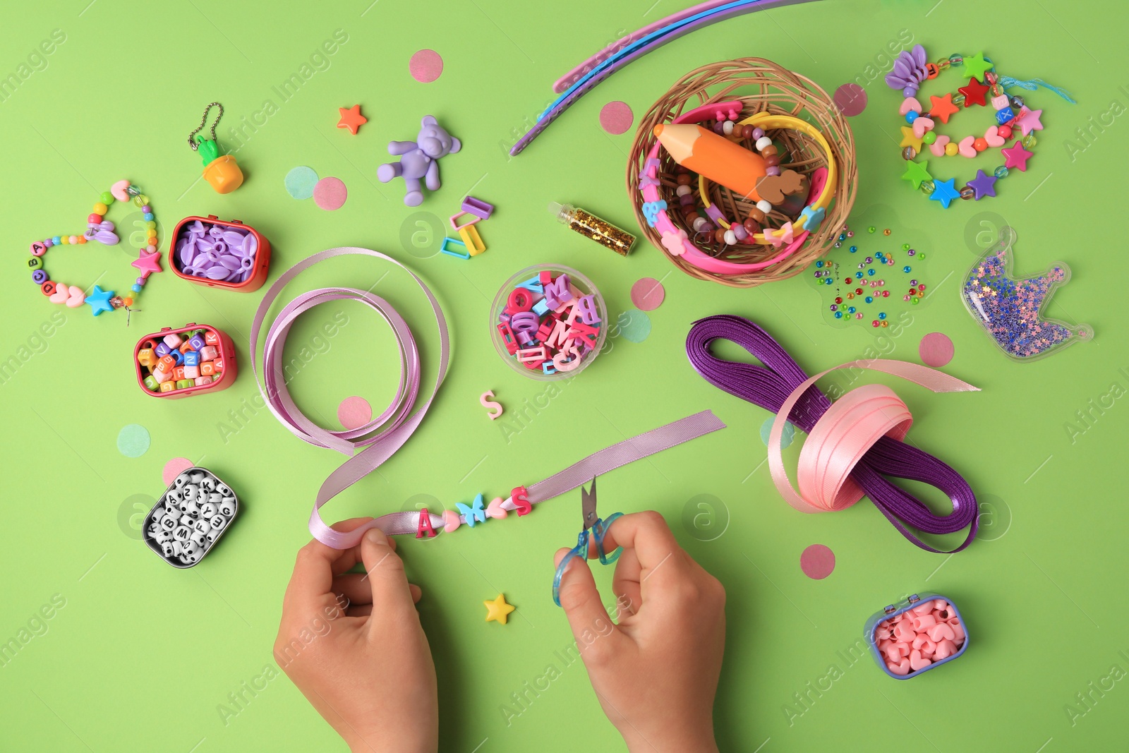 Photo of Child making beaded jewelry and different supplies on green background, top view. Handmade accessories