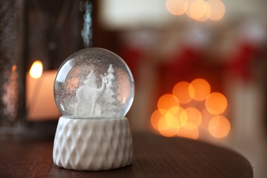 Snow globe on wooden table against blurred background, space for text. Bokeh effect