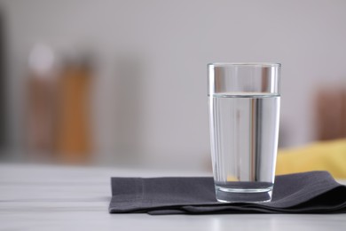 Photo of Glass of water and napkin on white table against blurred background. Space for text