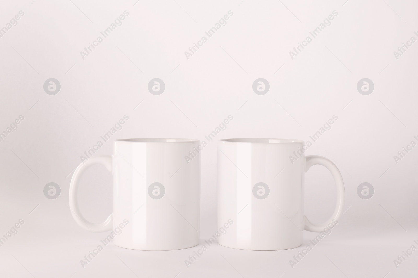 Blank white ceramic mugs on light background Photo of Blank white ceramic mugs on light background