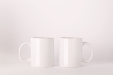 Photo of Blank white ceramic mugs on light background