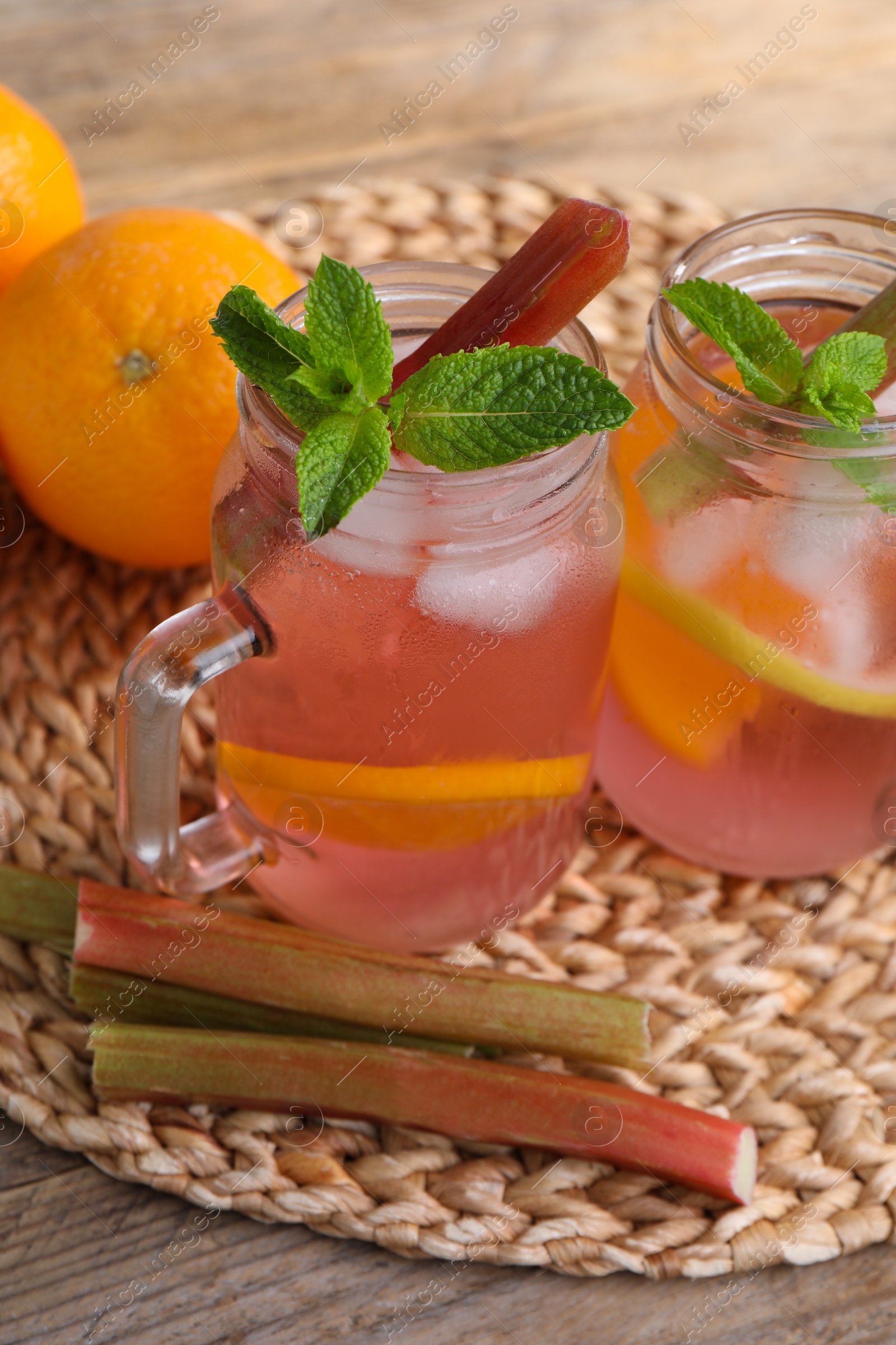 Photo of Mason jars of tasty rhubarb cocktail with citrus fruits on table