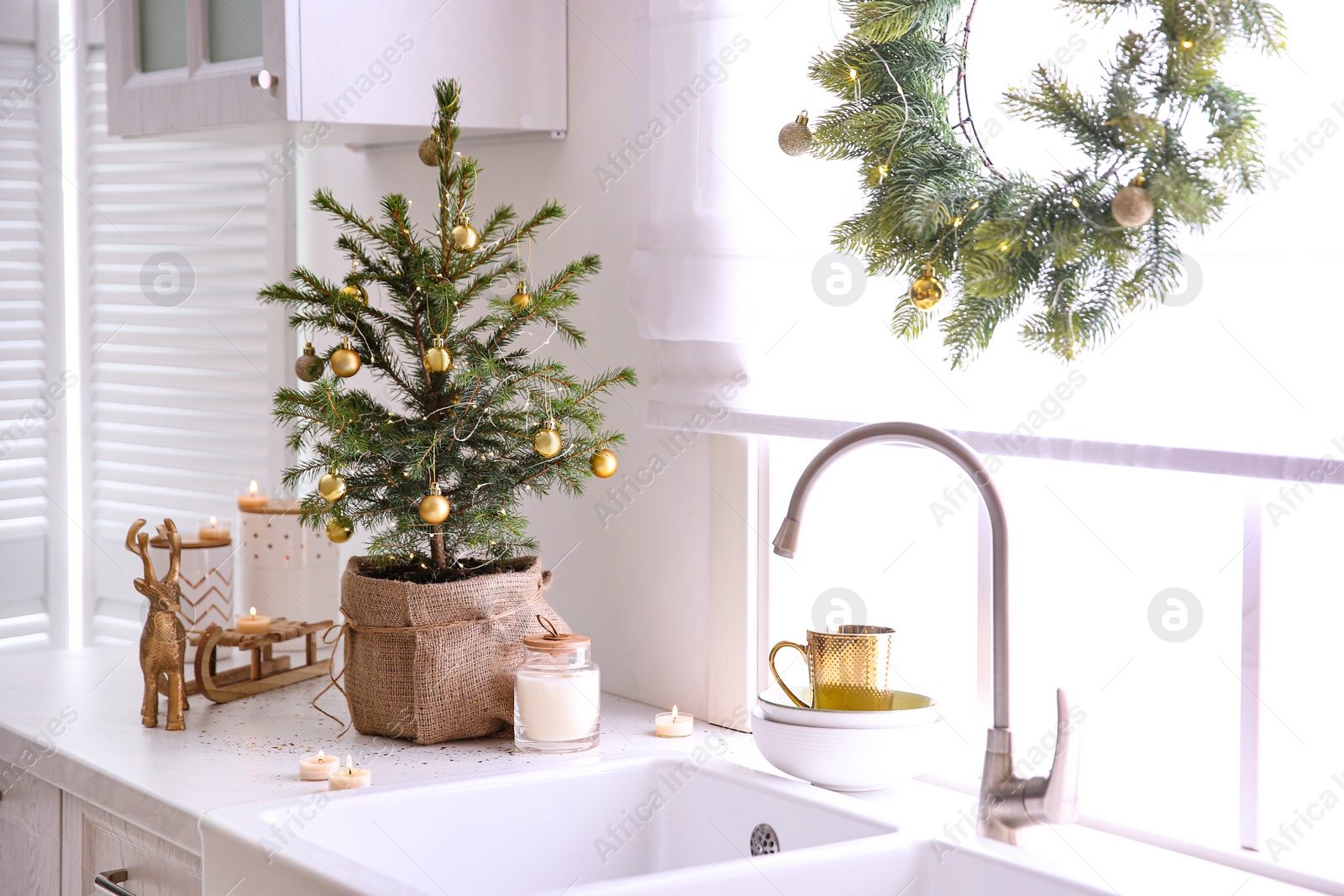 Photo of Small Christmas tree decorated with baubles and festive lights in kitchen