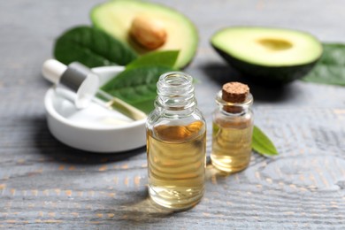 Bottles of essential oil and fresh avocado on grey wooden table