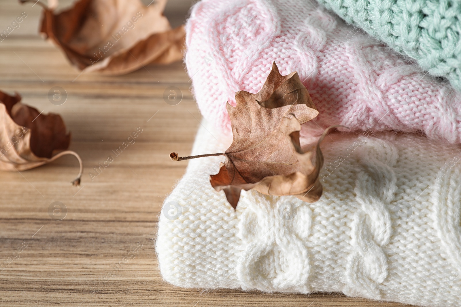 Image of Stack of folded warm sweaters with dry leaves on wooden table, closeup