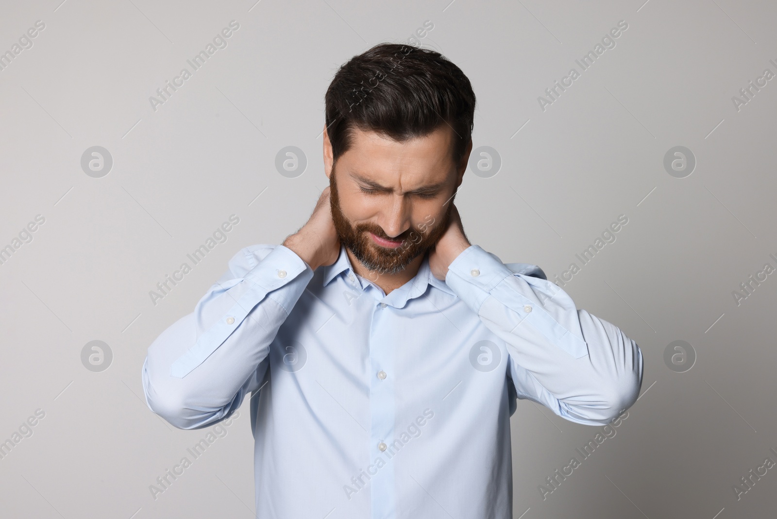 Photo of Man suffering from pain in his neck on light background. Arthritis symptoms