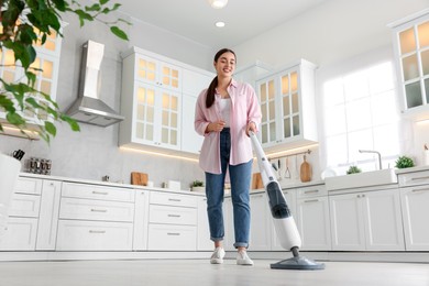 Photo of Happy woman cleaning floor with steam mop in kitchen at home, low angle view