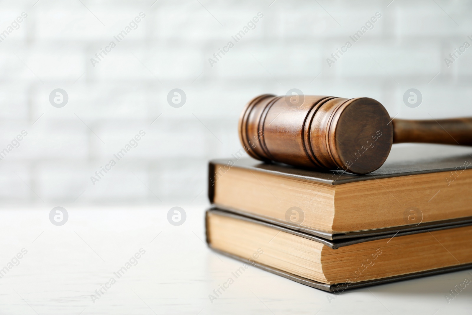 Photo of Wooden gavel and books on table against brick wall. Law concept