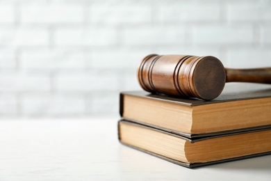 Wooden gavel and books on table against brick wall. Law concept