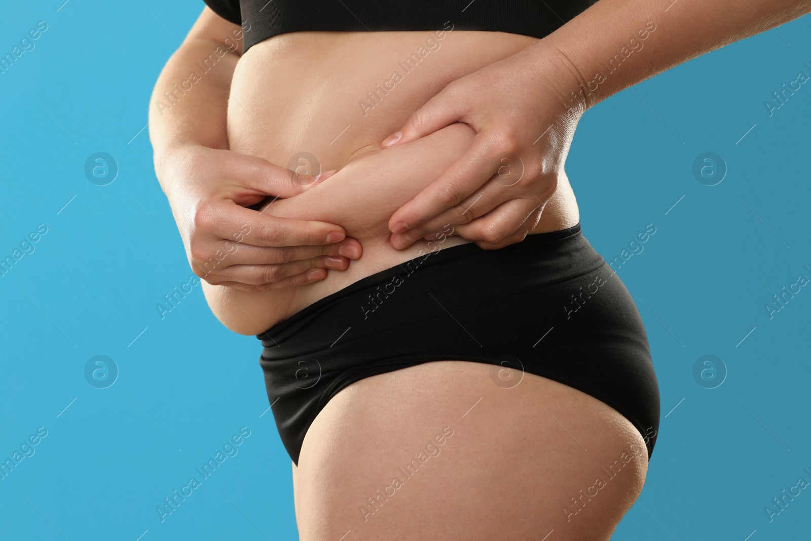 Photo of Woman touching belly fat on light blue background, closeup. Overweight problem