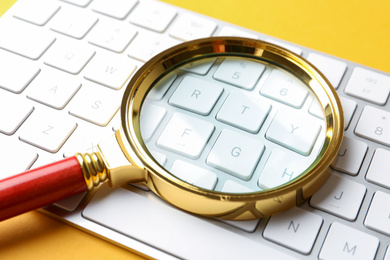 Photo of Magnifier glass and keyboard on orange background, closeup. Find keywords concept
