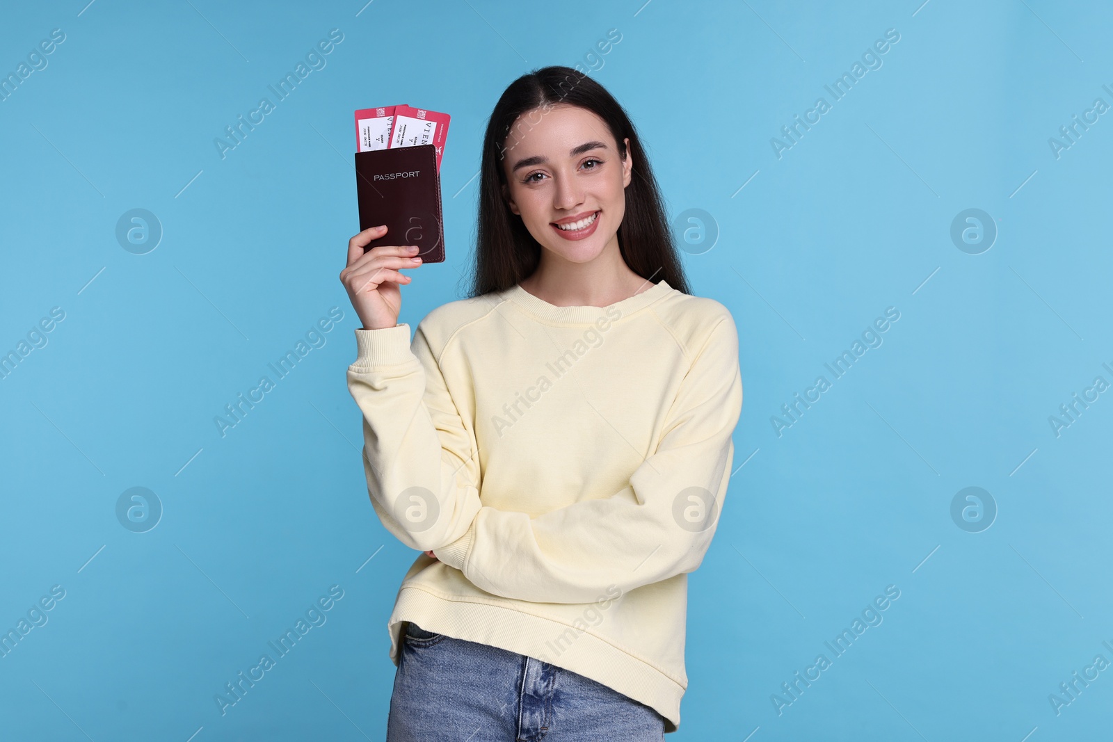 Photo of Smiling woman with passport and tickets on light blue background