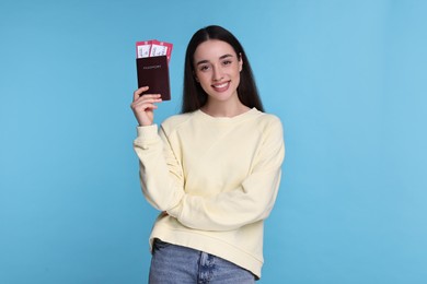 Smiling woman with passport and tickets on light blue background