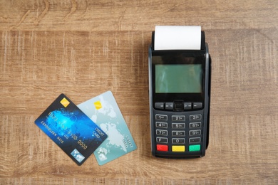 Photo of Modern payment terminal and credit cards on wooden background, top view. Space for text