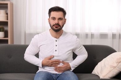 Photo of Man suffering from stomach pain on sofa at home