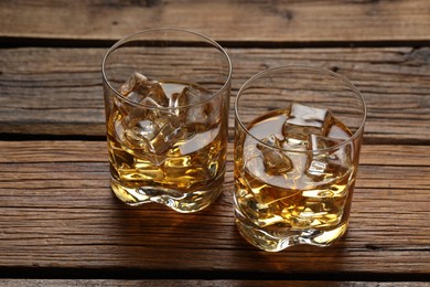 Photo of Whiskey with ice cubes in glasses on wooden table