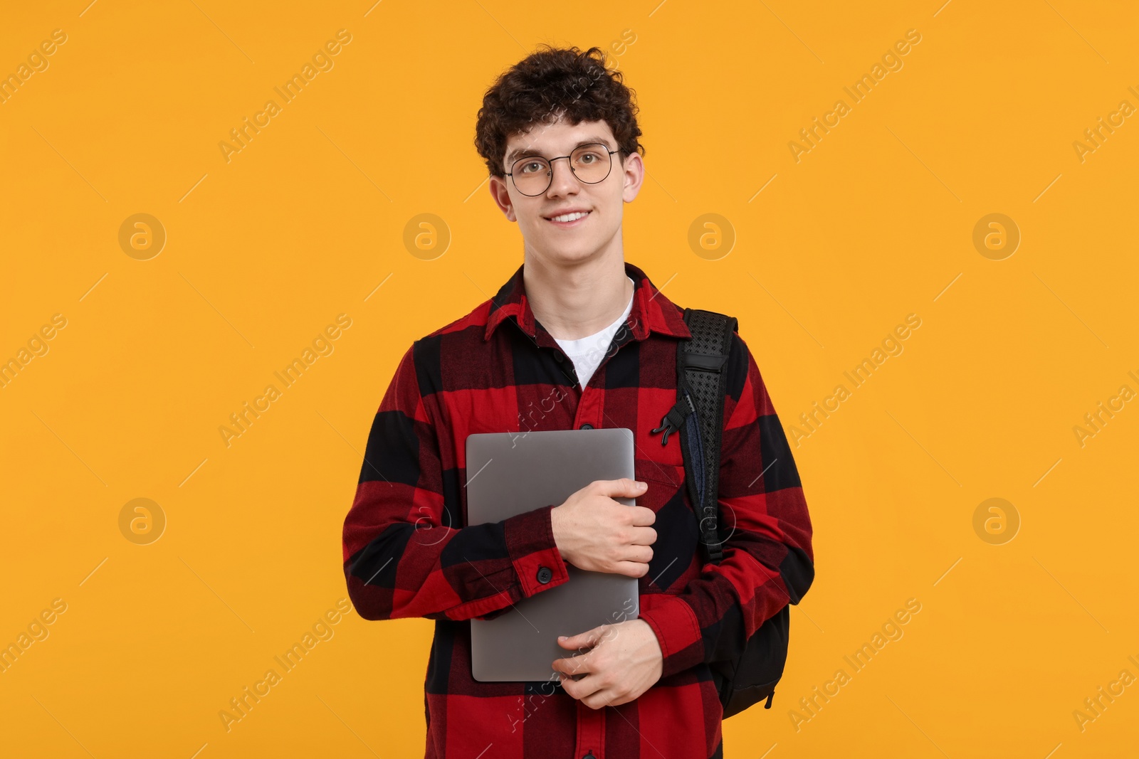 Photo of Portrait of student with backpack, laptop and glasses on orange background