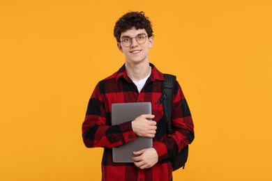 Portrait of student with backpack, laptop and glasses on orange background