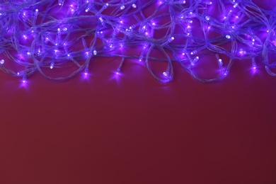 Photo of Glowing Christmas lights on burgundy background, top view. Space for text