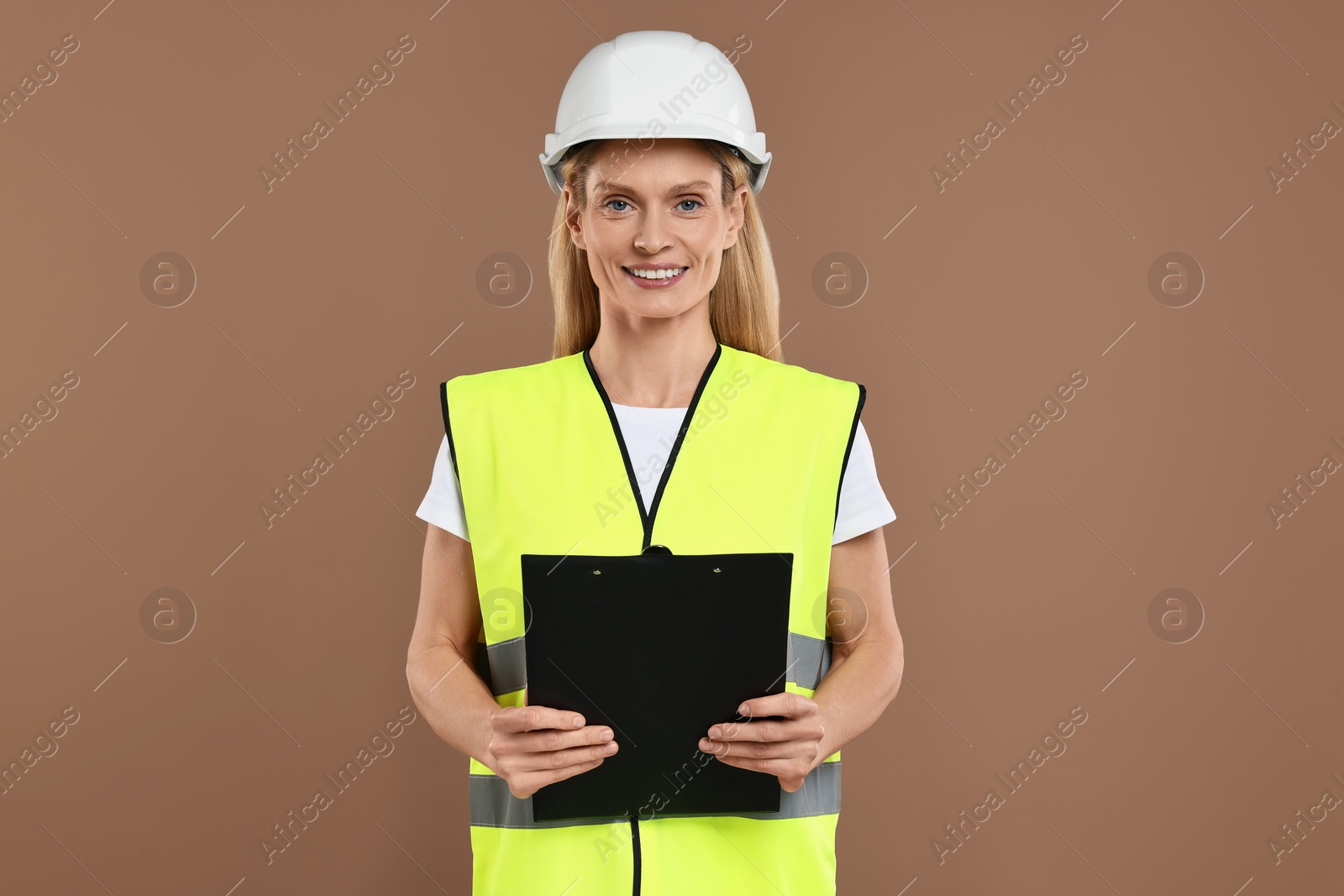 Photo of Engineer in hard hat holding clipboard on brown background