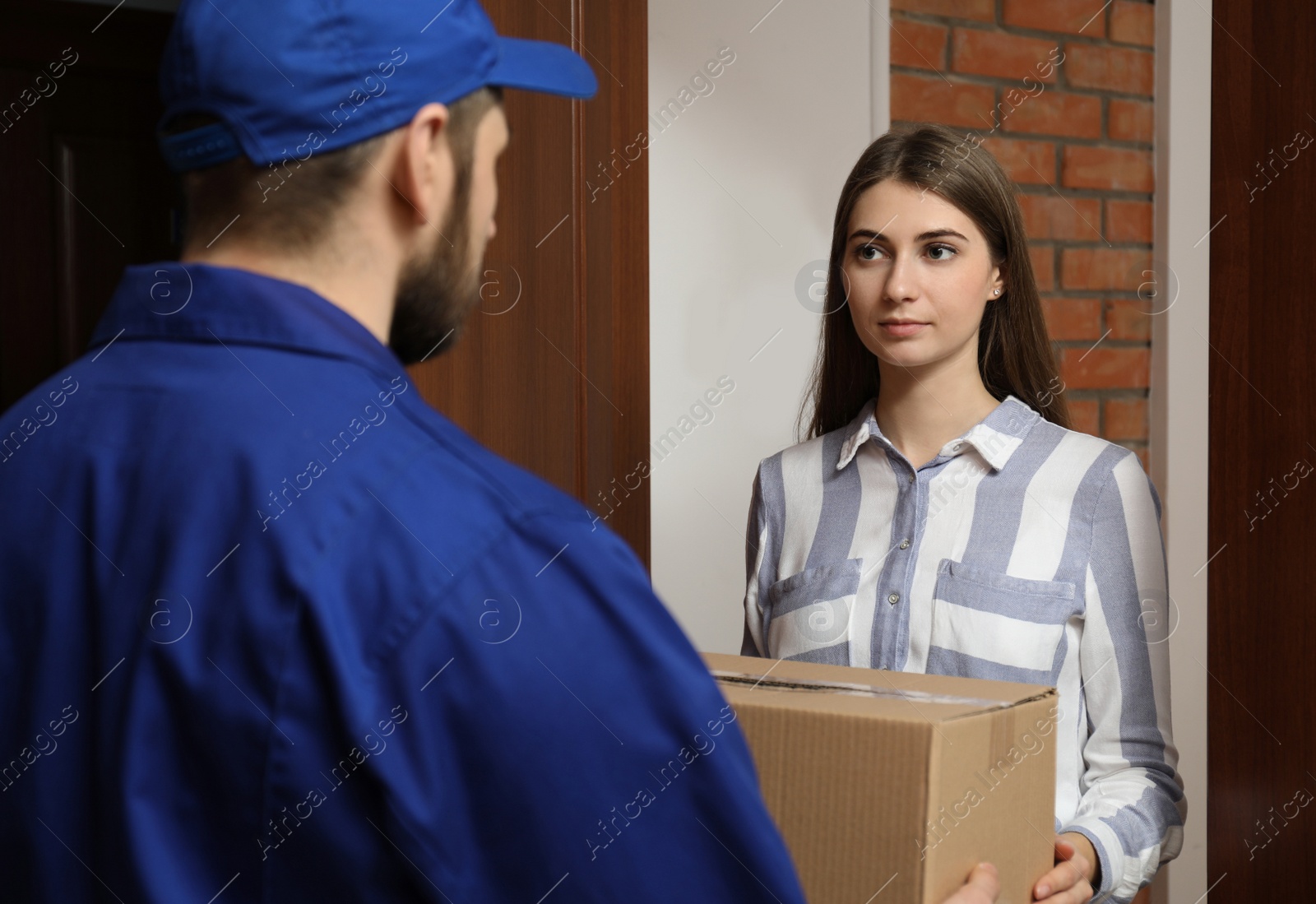 Photo of Young woman receiving parcel from delivery man indoors
