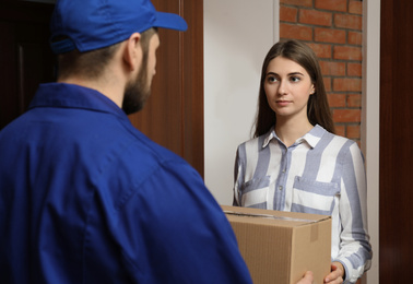 Photo of Young woman receiving parcel from delivery man indoors