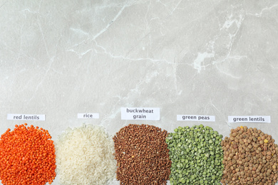 Flat lay composition with different types of legumes and cereals on grey marble table, space for text. Organic grains