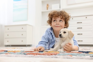 Photo of Little boy lying with cute puppy on carpet at home. Space for text