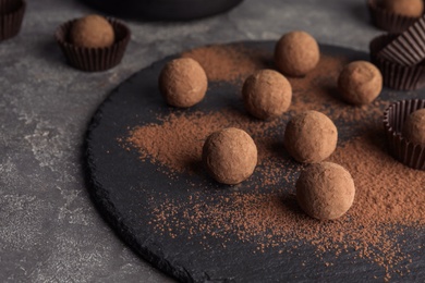 Photo of Slate plate with chocolate truffles on grey background, space for text