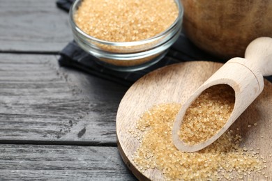 Brown sugar in bowl and scoop on black wooden table, closeup. Space for text