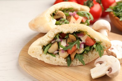 Delicious pita sandwiches with cheese, mushrooms tomatoes and arugula on white table