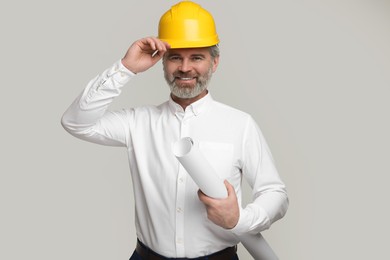 Architect in hard hat holding draft on grey background